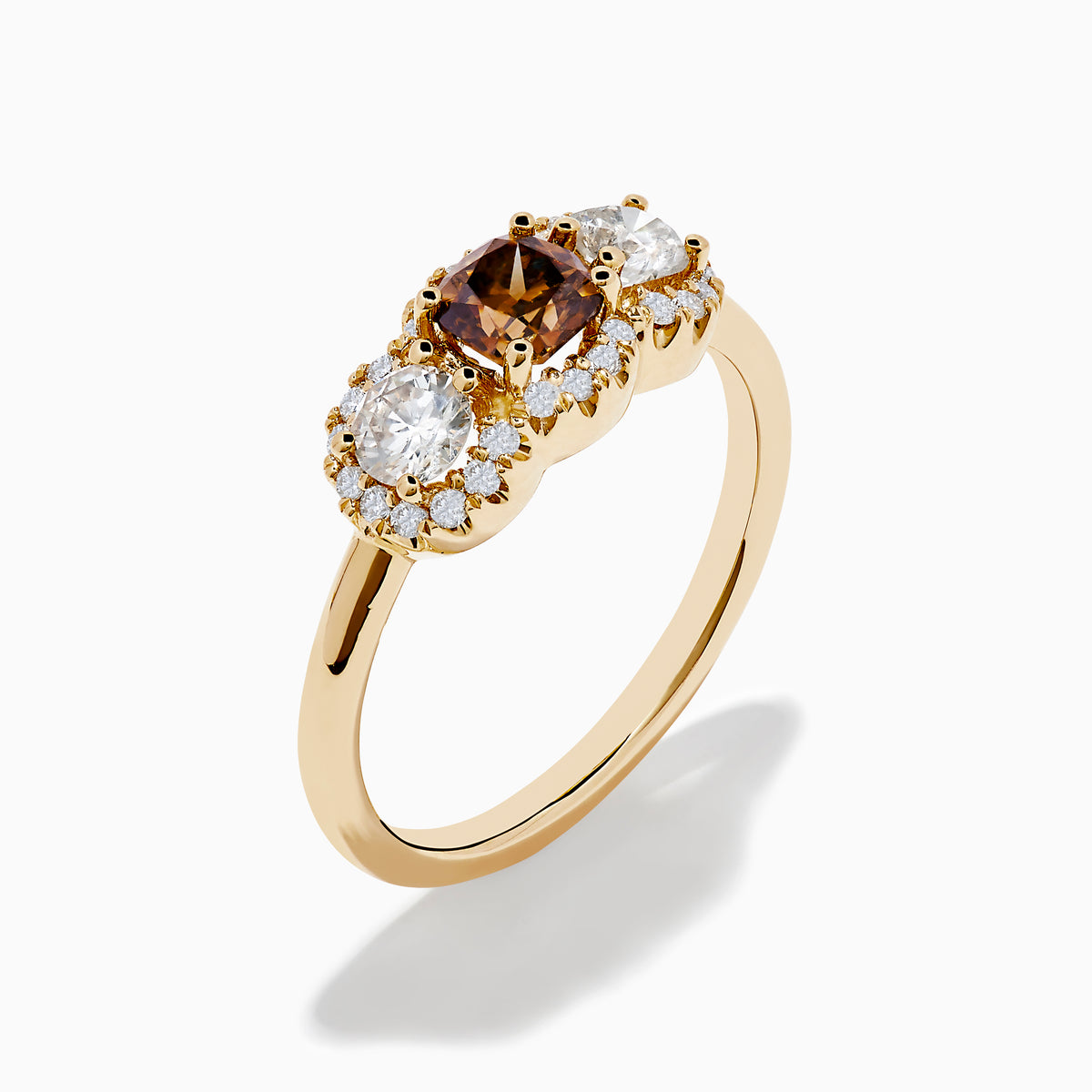 The Espresso 14K Yellow Gold Brown Diamond 3-Stone Ring features a central brown diamond, two oval white stones, and sparkling halo accents for a stunning look.