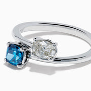 The Bella Bleu 14K White Gold Bypass Ring showcases a blue stone and a light brown diamond set side by side in prongs, displayed against a plain white background.