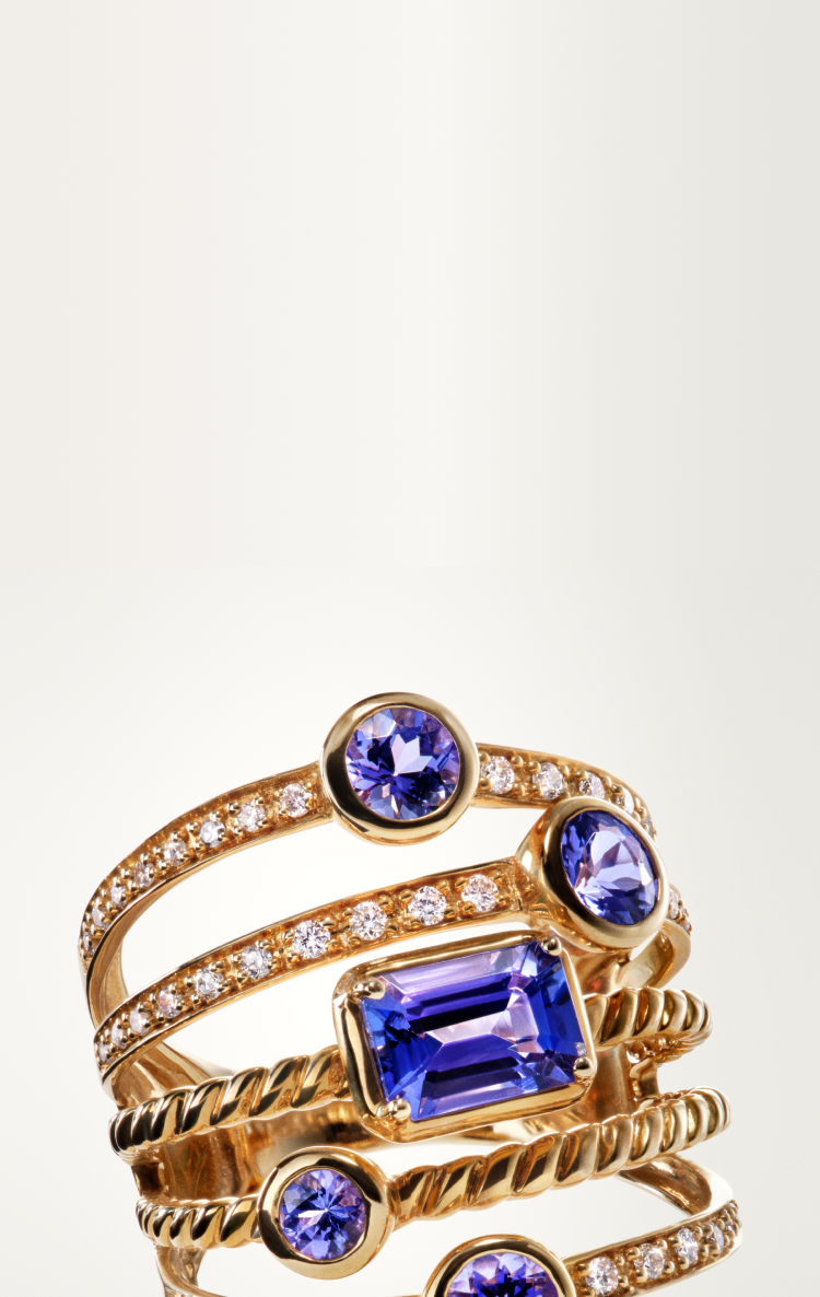 A stack of gold rings featuring blue gemstones and small clear diamonds, arranged in an elegant, intertwined design against a light background.