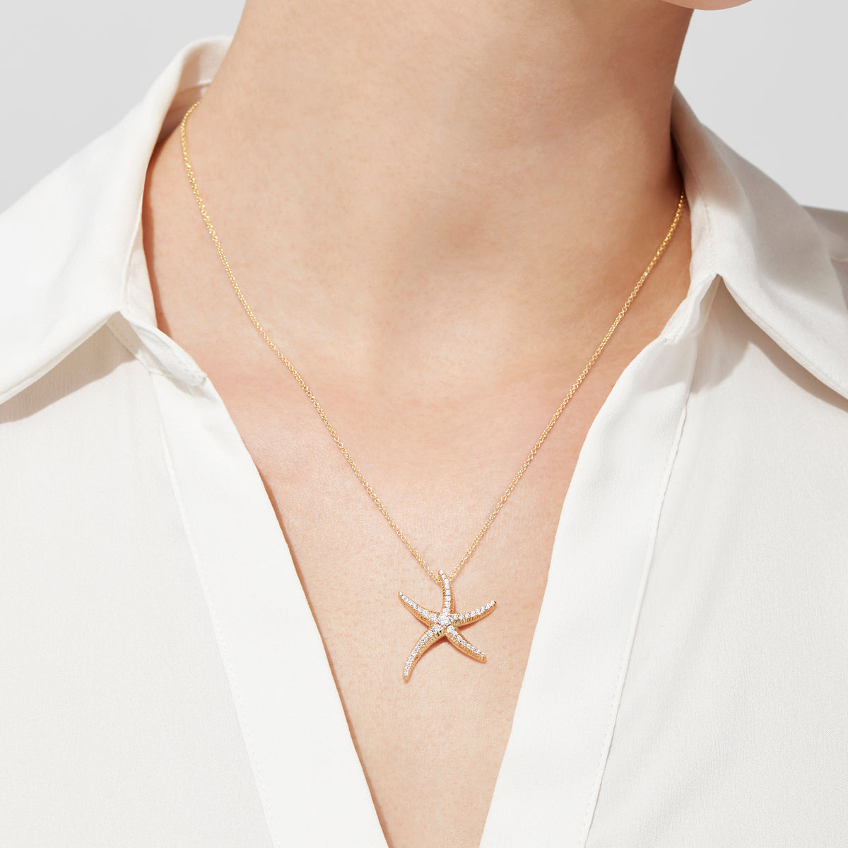 A woman in a white collared blouse showcases the DOro 14K Yellow Gold Diamond Starfish Pendant, 0.51 TCW. The image focuses on her neck and upper chest, highlighting the pendant’s sparkling diamonds.