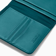 Teal Vegan Leather Passport Holder open to display card slots on the left, a transparent ID section in the center, and a larger pocket on the right, all crafted from vegan leather against a white background.
