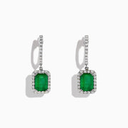 The 14K White Gold Emerald and Diamond Drop Earrings, 2.30 TCW, feature emerald-cut green emeralds surrounded by diamonds and suspended from diamond-studded drops, shown on a white background.