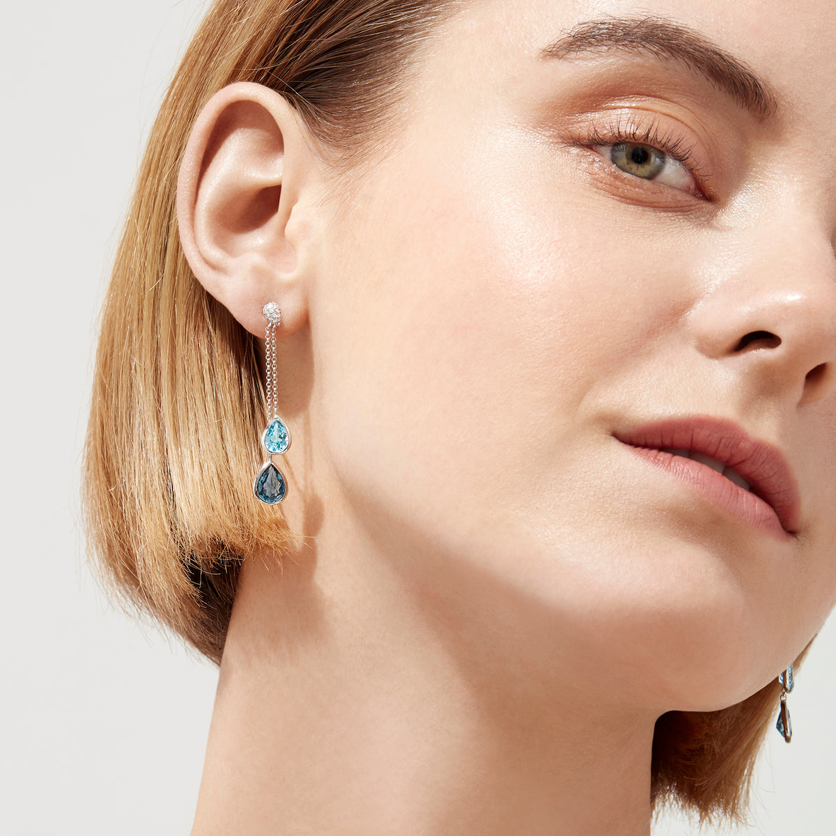 The Ocean Bleu 14K White Gold Blue Topaz and Diamond Earrings (4.28 TCW) feature elegant blue topaz teardrops, delicate chains, and round diamond accents, inspired by classic diamond earring designs.