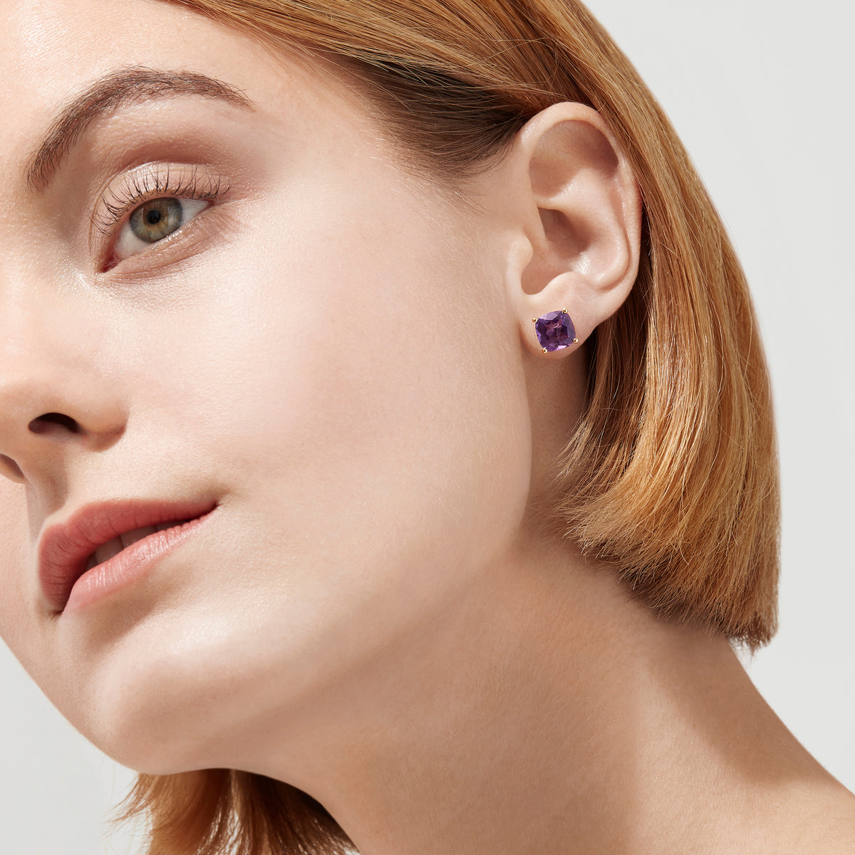A pair of 14K Yellow Gold Amethyst Stud Earrings, 4.25 TCW, with cushion-cut gems set in prongs, displayed against a plain white background.