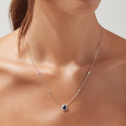 The Royale Bleu 14K White Gold Sapphire and Diamond Necklace, 1.11 TCW, features a round blue sapphire pendant with a halo of clear stones and two diamonds set along each side of the chain.