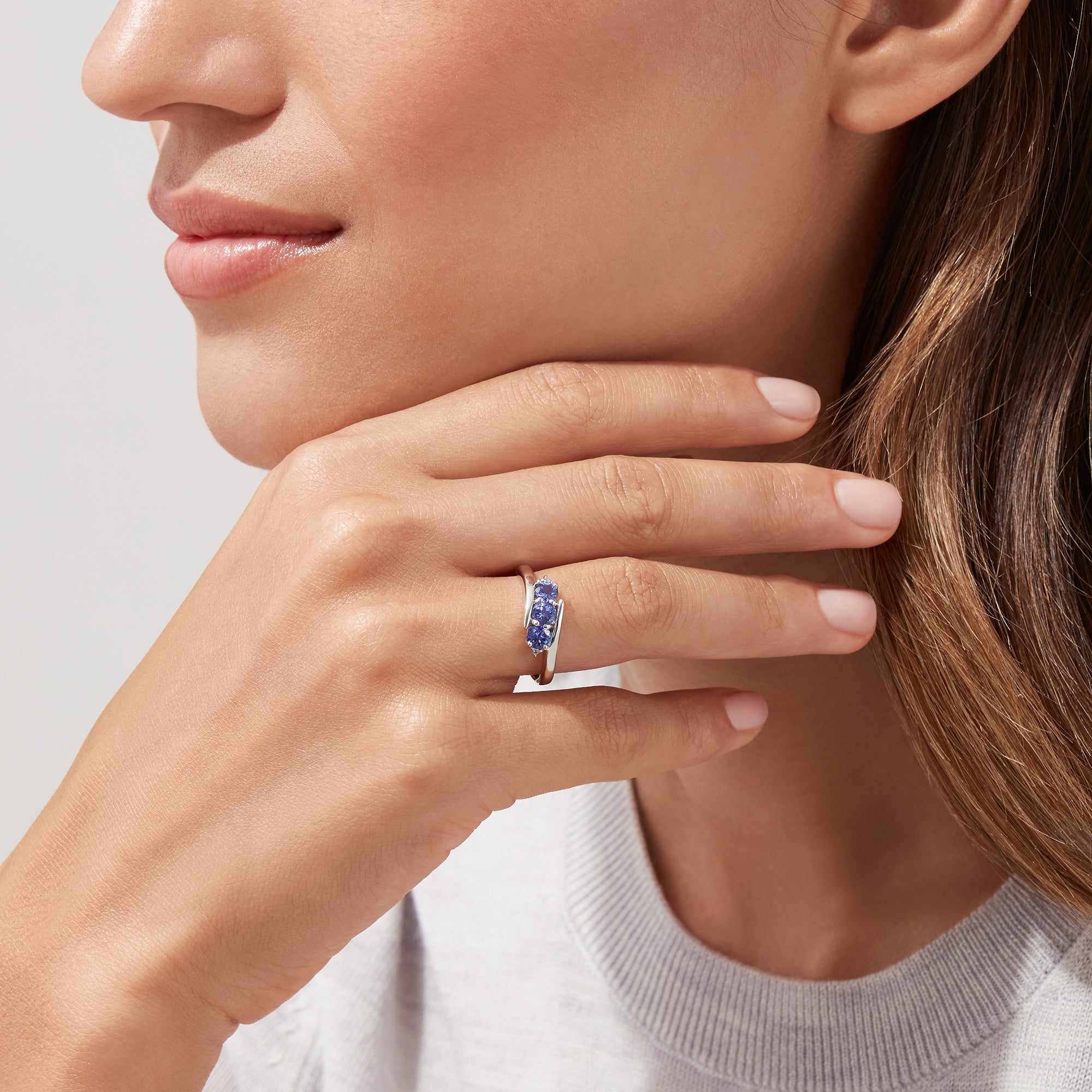 The Nahla Siri Sterling Silver Tanzanite and Diamond Ring (0.86 TCW) showcases three round tanzanites set side by side in a modern overlapping band, displayed on a white background.