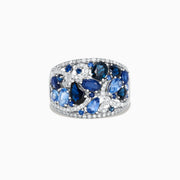 The 14K White Gold Blue Sapphire and Diamond Ring, 4.01 TCW, features sapphires in varied shapes and blue shades with sparkling white diamonds, all set in an intricate swirling design.