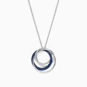 A 14K white gold necklace showcases a pendant of two interlocking circles—one with blue sapphires, the other with diamonds (0.74 TCW)—suspended from a delicate chain on a white background.