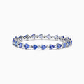 The Nahla 14K White Gold Tanzanite and Diamond Tennis Bracelet features alternating triangular tanzanite stones and round diamonds in a delicate, repeating pattern against a plain white backdrop.