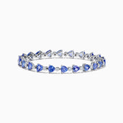 The Nahla 14K White Gold Tanzanite and Diamond Tennis Bracelet features alternating triangular tanzanite stones and round diamonds in a delicate, repeating pattern against a plain white backdrop.