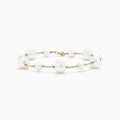 The 14K Yellow Gold Pearl Station Bracelet features round white pearls of varying sizes, evenly spaced along the gold chain, and is displayed on a plain white background.
