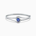 The Nahla Siri 14K White Gold Tanzanite and Diamond Bangle, 2.61 TCW, showcases a central round tanzanite gemstone encircled by sparkling diamonds on a sleek, open band design.