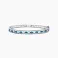 The Bella Bleu 14K White Gold Blue and White Diamond Bangle, 1.27 TCW, features a row of oval blue and white diamonds between two lines of small white crystals, shown on a white background.