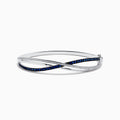 The Royale Bleu 14K White Gold Blue Sapphire and Diamond Crossover Bangle showcases a modern, elegant design with sparkling diamonds and a row of blue sapphires for a sophisticated accessory.
