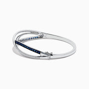 The Royale Bleu 14K White Gold Blue Sapphire and Diamond Crossover Bangle showcases a modern, elegant design with sparkling diamonds and a row of blue sapphires for a sophisticated accessory.