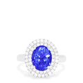 The 14K White Gold Tanzanite and Diamond Ring, 3.13 TCW features a large oval blue tanzanite center stone encircled by two rows of round diamonds in a dazzling halo setting.