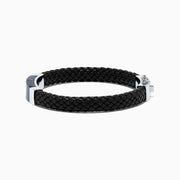 The Mens Sterling Silver Pietersite Woven Leather Bracelet, 12.50 TCW, features black woven leather, a sterling silver clasp, and a rectangular silver accent with a dark blue pietersite marbled center, shown on a white background.