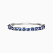 The Nahla Siri 14K White Gold Tanzanite Diamond Bangle, 4.76 TCW, features a row of blue triangle-cut tanzanite gems set between small diamonds along the top half of the band.