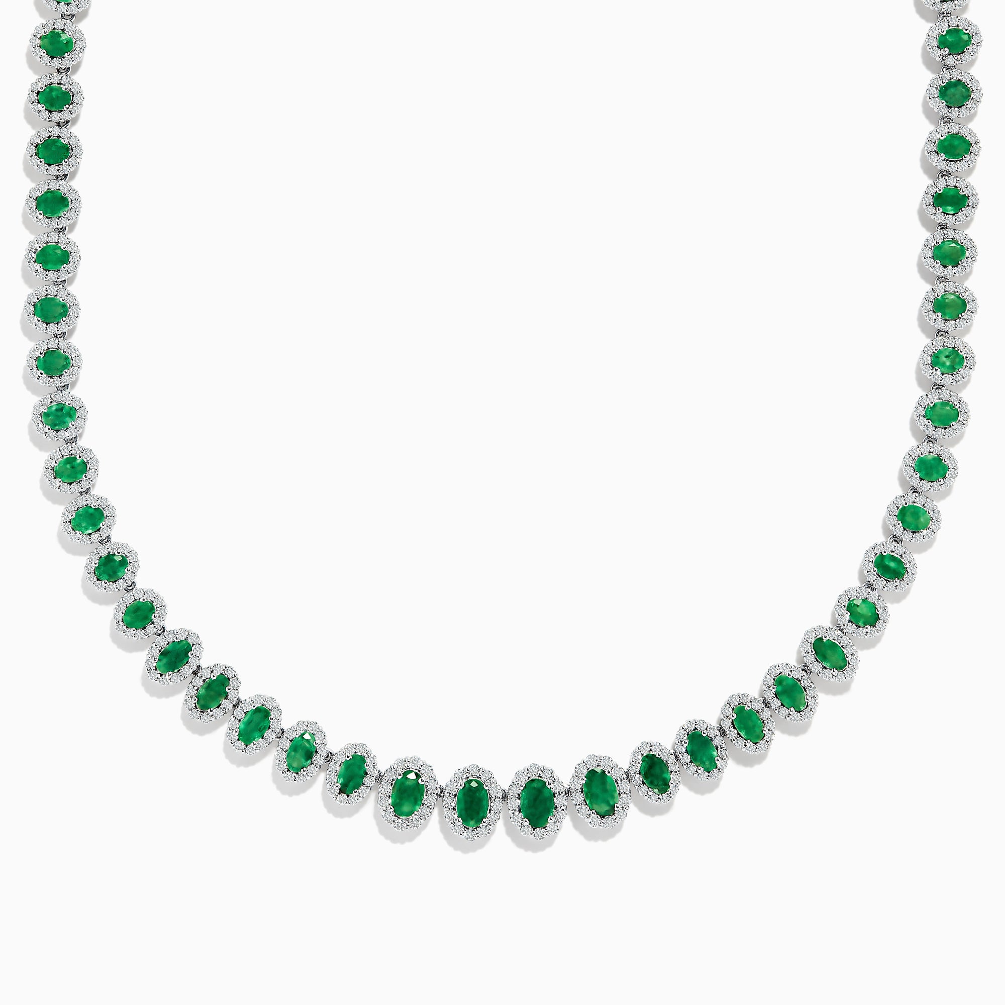 The 14K White Gold Emerald and Diamond Tennis Necklace showcases oval green emeralds, each surrounded by sparkling diamonds, evenly set along a white gold chain displayed on a white background.