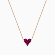 The 14K Rose Gold Ruby Pave Heart Necklace features a heart-shaped pendant encrusted with sparkling rubies on a delicate rose gold chain, displayed against a plain white background.