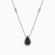 The 14K White Gold Black and White Diamond Pear Shaped Necklace, 1.09 TCW, features a teardrop pendant with black and white diamonds at the center, haloed by clear stones, plus two small clear stones set along the chain.