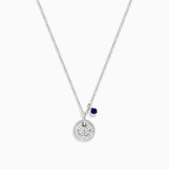 The Seaside Sterling Silver Sapphire and Diamond Anchor Necklace features a round, crystal-studded anchor pendant with a small dark blue sapphire charm, elegantly displayed on a white background.