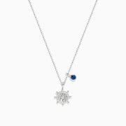The Seaside Sterling Silver Diamond and Sapphire Ship Wheel Pendant features a ship wheel design with diamond accents and a sapphire charm, showcased on a sterling silver chain against a white background.