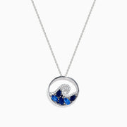 The Seaside 14K White Gold Blue Sapphire and Diamond Wave Pendant is a silver necklace featuring a circular pendant with blue sapphires and diamonds, reflecting the beauty of ocean waves and foam.