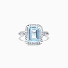 The Aquarius 14K White Gold Aquamarine and Diamond Ring, 3.33 TCW, features a large emerald-cut aquamarine surrounded by a diamond halo and set on a diamond-studded band, shown on a white background.