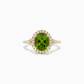 The 14K Yellow Gold Peridot and Diamond Ring showcases an oval-cut green peridot center, encircled by a halo of round white diamonds, with extra diamonds set along the band.