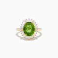The 14K Yellow Gold Peridot and Diamond Ring features an oval peridot at the center, surrounded by a halo of baguette-cut diamonds, shown on a white background.