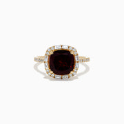 The 14K Yellow Gold Garnet and Diamond Ring features a cushion-cut deep red garnet center, surrounded by a halo of baguette and round white diamonds, with more diamonds set along the band.