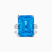 The 14K White Gold Blue Topaz and Diamond Ring, 29.29 TCW, features a large rectangular emerald-cut blue topaz accented by small white diamonds, shown on a white background.