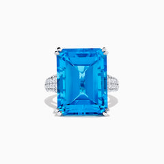 The 14K White Gold Blue Topaz and Diamond Ring, 29.29 TCW, features a large rectangular emerald-cut blue topaz accented by small white diamonds, shown on a white background.
