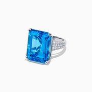 The 14K White Gold Blue Topaz and Diamond Ring, 29.29 TCW, features a large rectangular emerald-cut blue topaz accented by small white diamonds, shown on a white background.