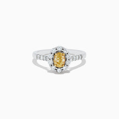 The 14K White Gold White and Fancy Yellow Diamond Ring, 1.10 TCW, features an oval yellow diamond center, haloed by clear round diamonds with more diamonds along the band—a timelessly elegant piece.