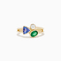 The 14K Yellow Gold Tri Stone Diamond, Emerald, and Tanzanite Ring features a split band with a round diamond, triangular tanzanite, and oval emerald arranged in an asymmetrical cluster.