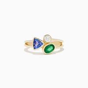 The 14K Yellow Gold Tri Stone Diamond, Emerald, and Tanzanite Ring features a split band with a round diamond, triangular tanzanite, and oval emerald arranged in an asymmetrical cluster.