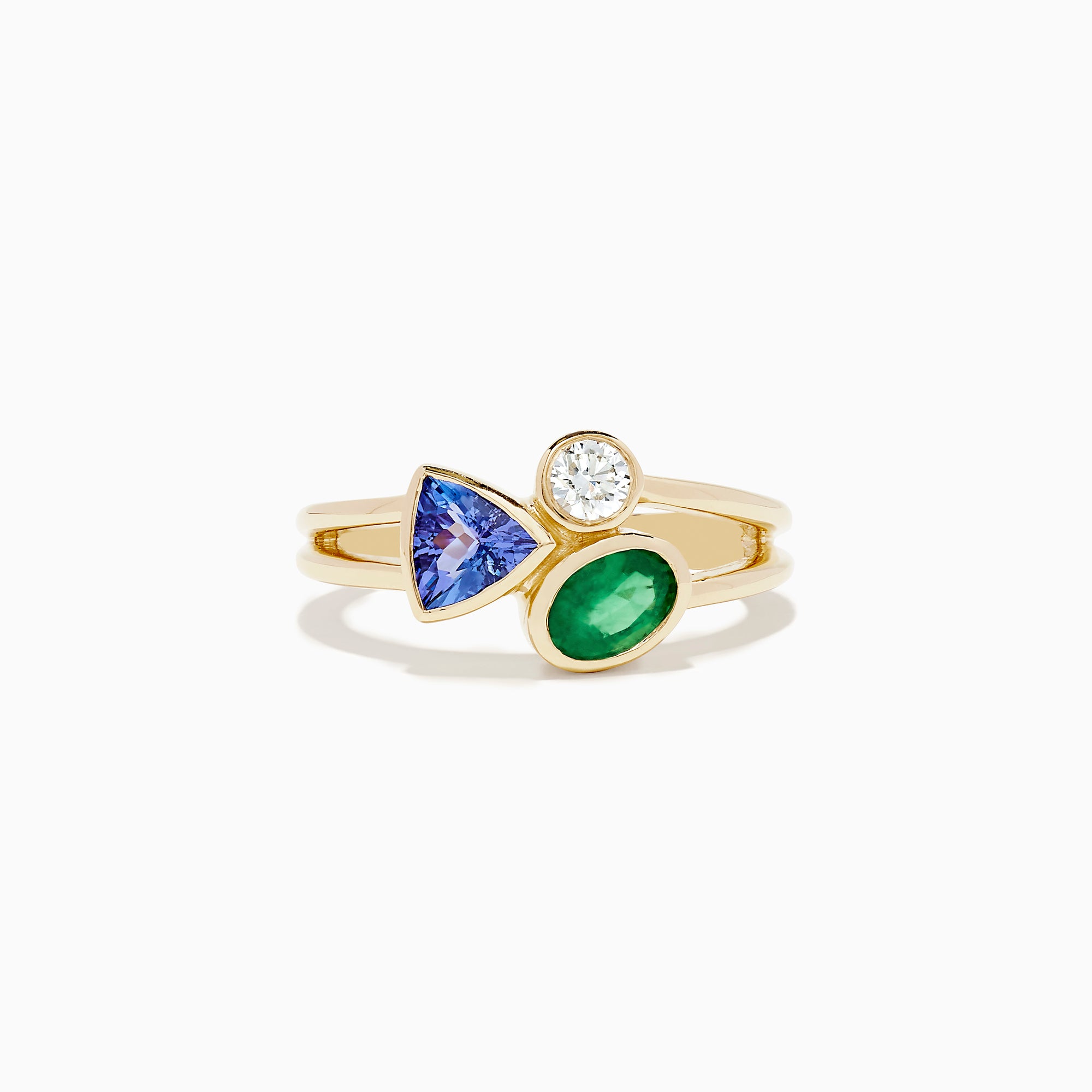 The 14K Yellow Gold Tri Stone Diamond, Emerald, and Tanzanite Ring features a split band with a round diamond, triangular tanzanite, and oval emerald arranged in an asymmetrical cluster.