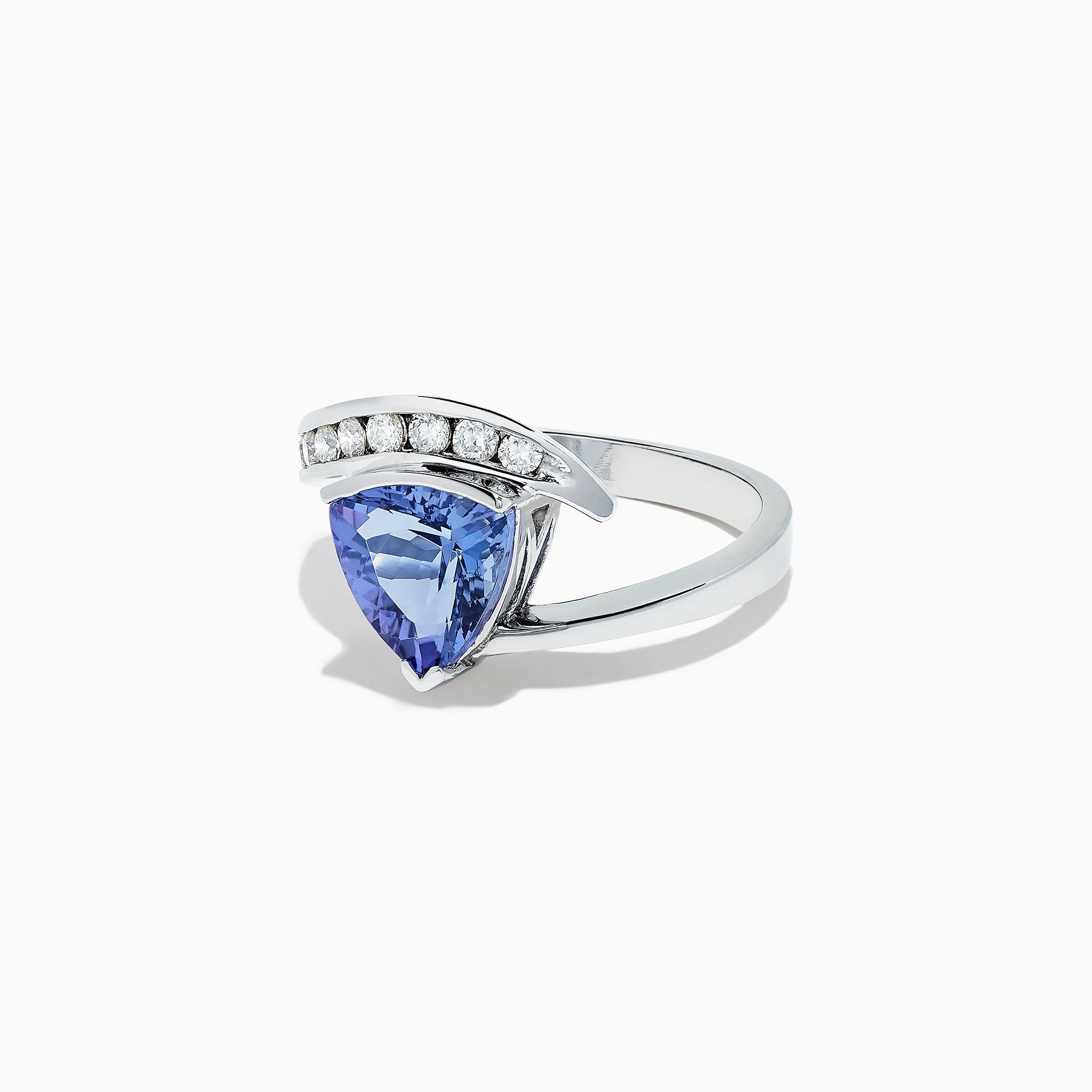 The Nahla Siri 14K White Gold Tanzanite and Diamond Ring, 1.88 TCW, showcases a large triangular blue tanzanite center with a curved band of round diamonds above it, set in an elegant modern design.