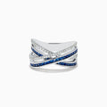 The 14K White Gold Blue Sapphire and Diamond Crossover Ring features overlapping bands adorned with sparkling diamonds and vivid blue sapphires in an elegant crisscross design, shown on a white background.