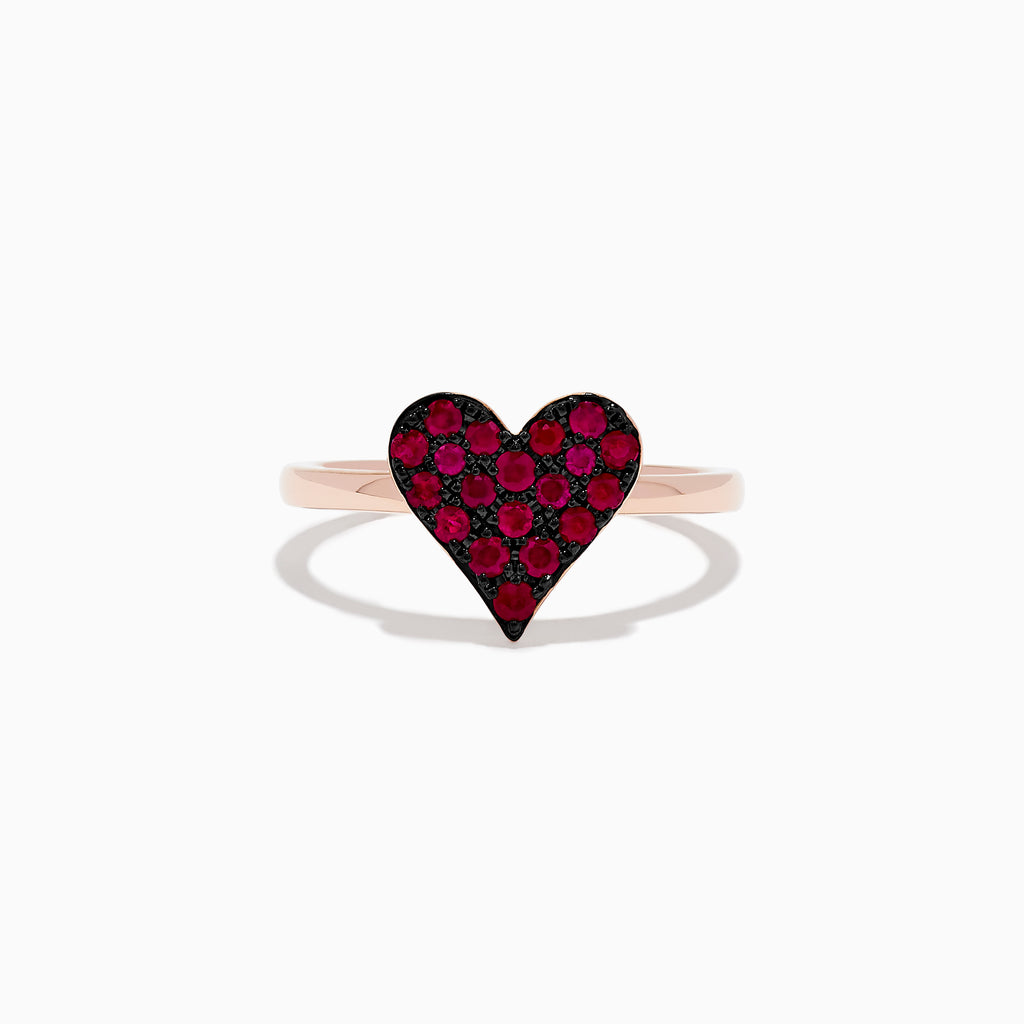 The 14K Rose Gold Ruby Heart Ring showcases a heart-shaped centerpiece with red gemstones, casting a gentle shadow on a white background.