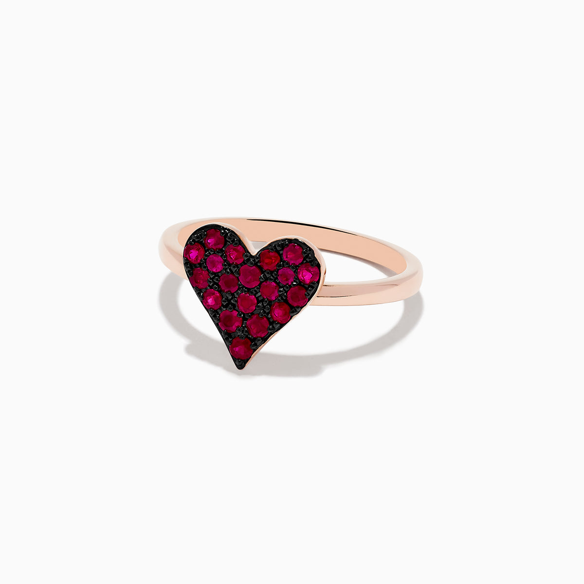 The 14K Rose Gold Ruby Heart Ring showcases a heart-shaped centerpiece with red gemstones, casting a gentle shadow on a white background.