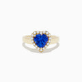 The Nahla Siri 14K Yellow Gold Tanzanite and Diamond Heart Ring, featuring a heart-shaped blue tanzanite surrounded by round white diamonds, is shown against a plain white background.