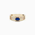The Royale Bleu 14K Yellow Gold Sapphire and Diamond Ring features a central oval blue sapphire accented by two rows of sparkling round diamonds on each side, beautifully set against a white gold background.